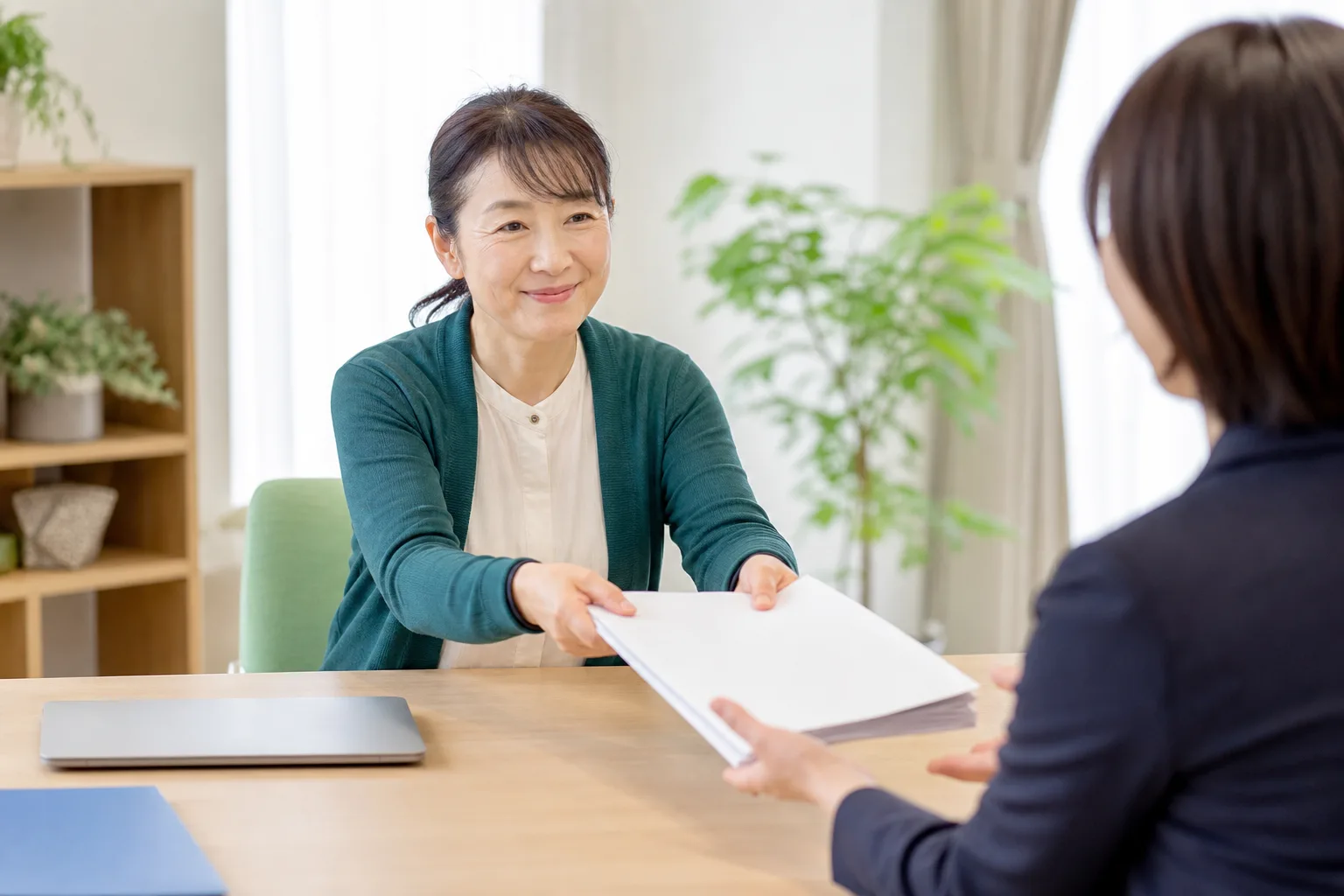 福祉事業所の管理者が、書類の束を打ち合わせ相手に手渡している様子