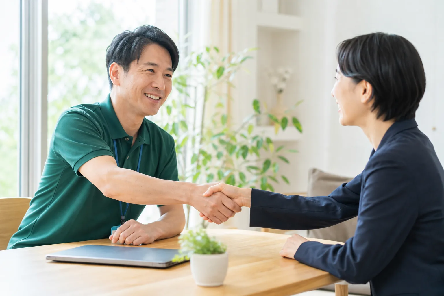 打ち合わせのテーブル越しに握手を交わす2人